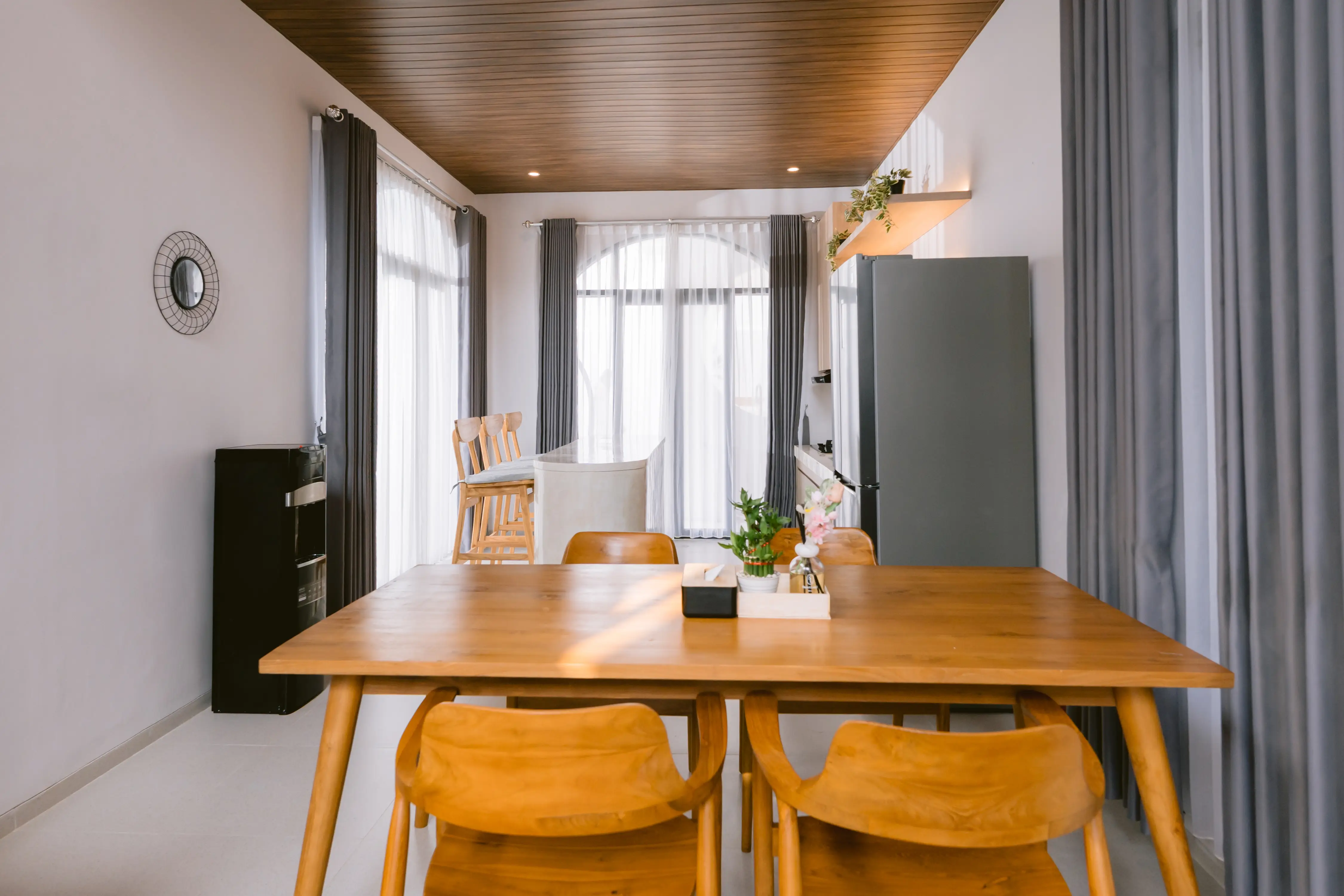 Long teak dining table with arched window beyond